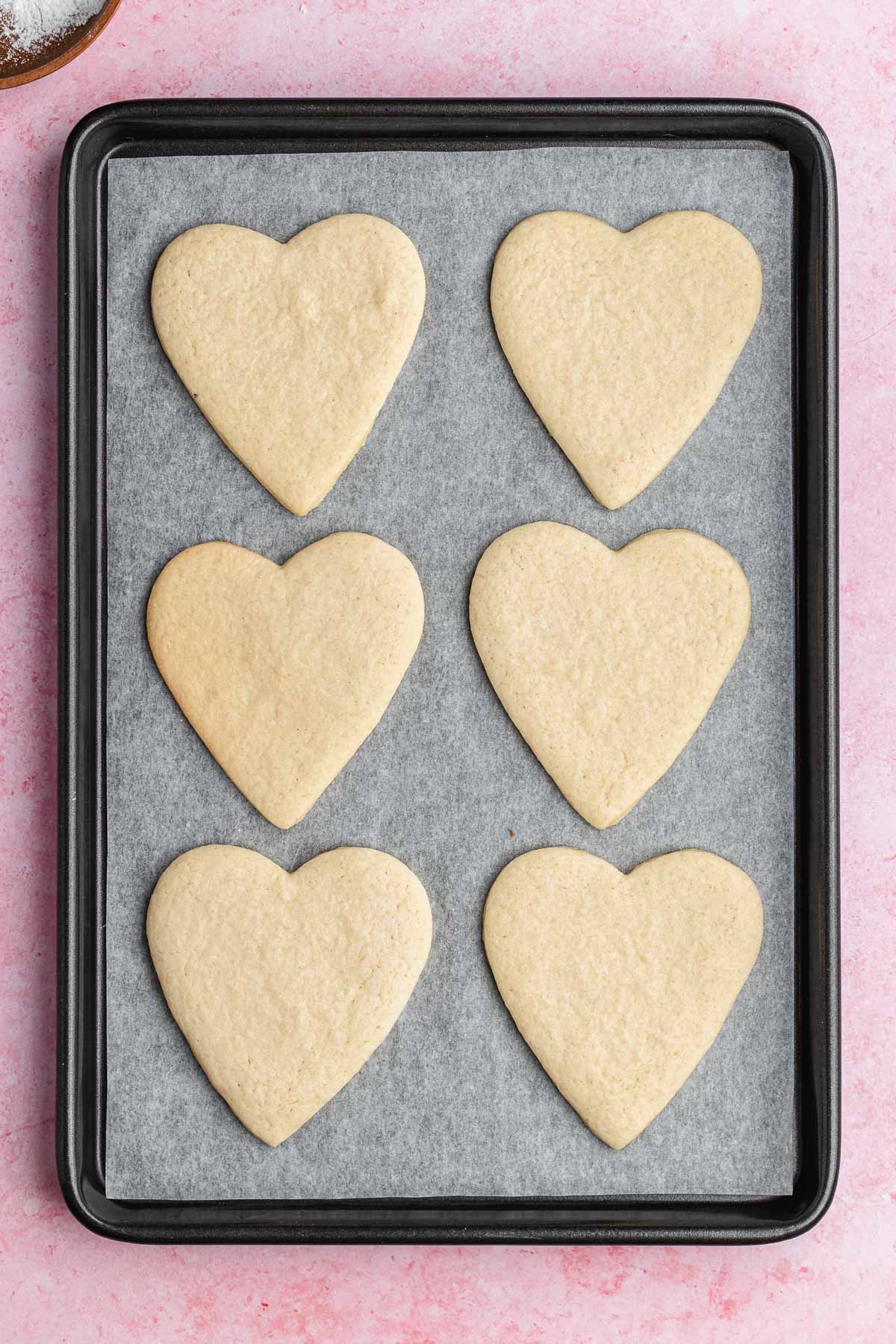 6 heart shaped cooked cookies on a baking sheet
