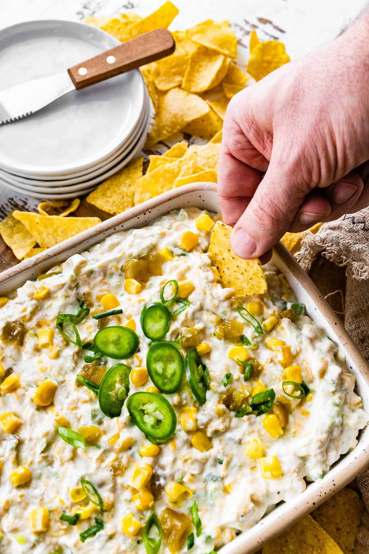 Corn Dip finished dip in serving dish garnished with sliced jalapeno and holding chip with dip on it.