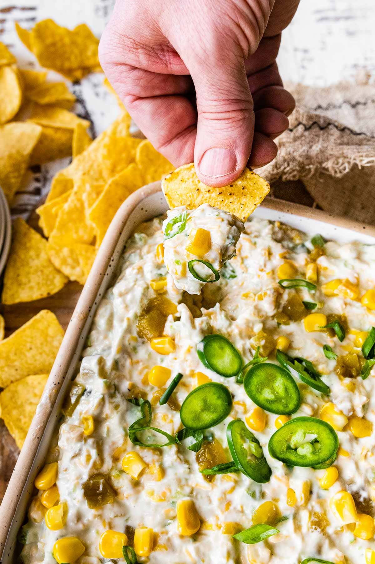 Corn Dip finished dip in serving dish garnished with sliced jalapeno and holding chip with dip on it.