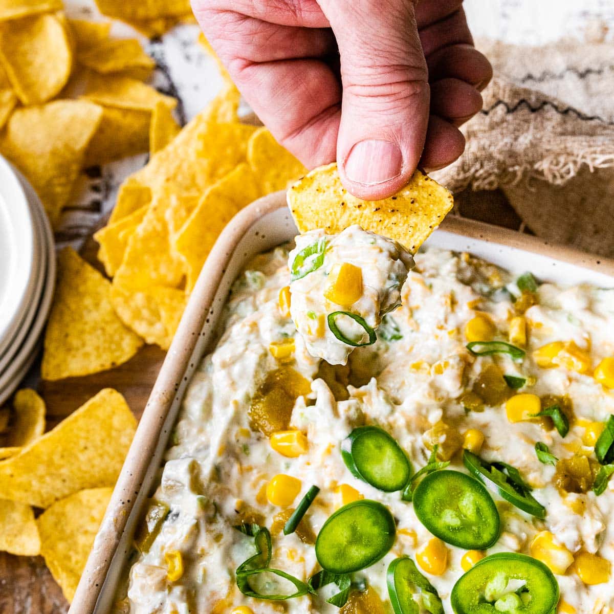 Corn Dip finished dip in serving dish garnished with sliced jalapeno and holding chip with dip on it.