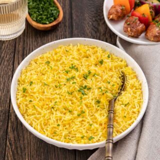 Saffron Rice finished rice with garnish in large bowl with spoon and kebabs on separate plate