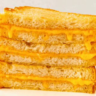 A Stack of cornered Sheet Pan Grilled Cheese Sandwiches stack vertically on a plate