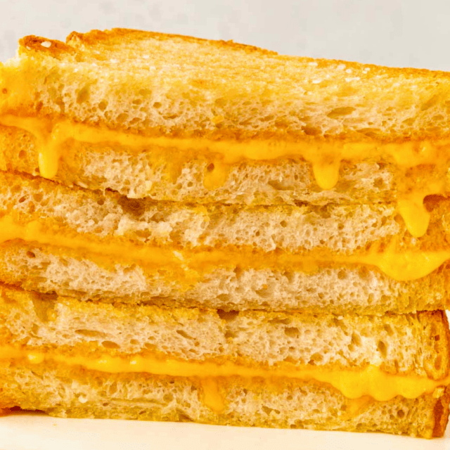 A Stack of cornered Sheet Pan Grilled Cheese Sandwiches stack vertically on a plate