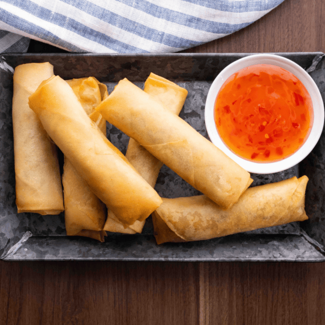 Fried spring rolls on platter with sweet and sour sauce in bowl