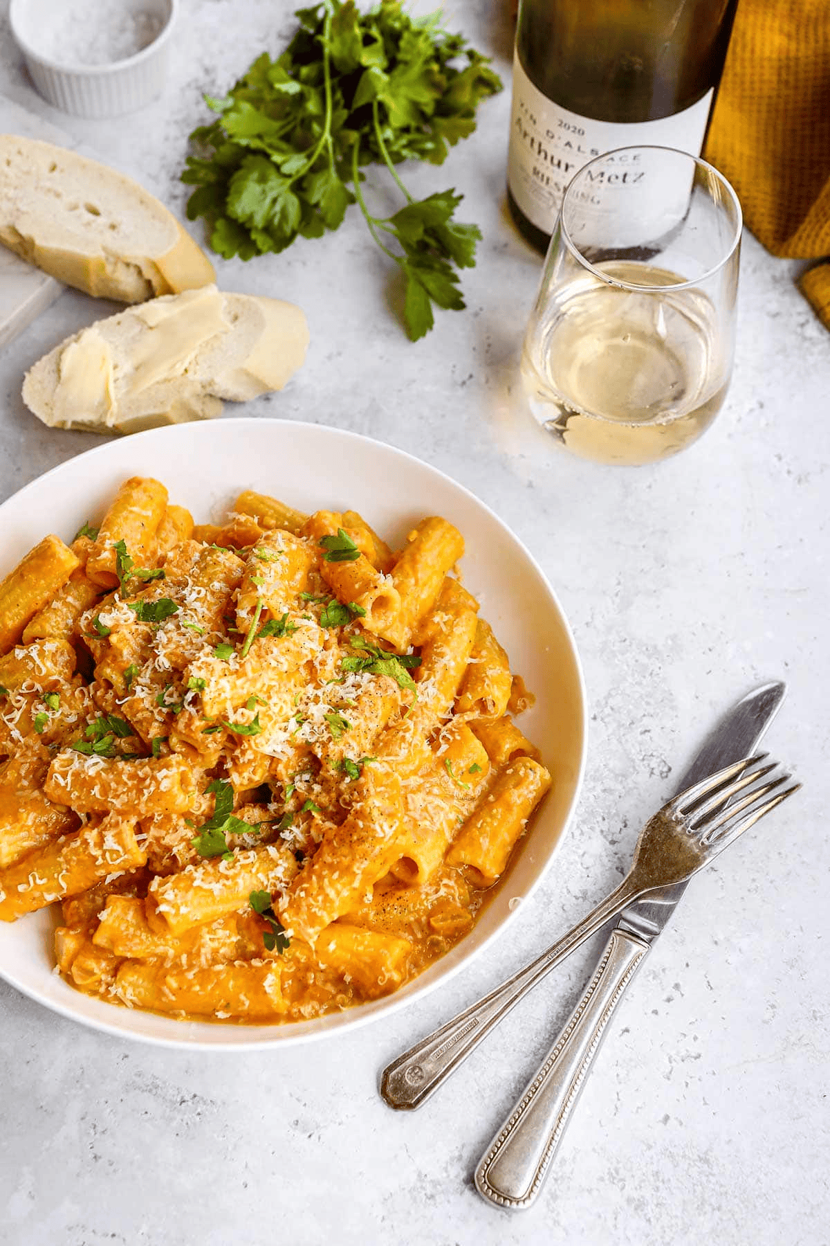 Serving of pasta with fork and knife, wine, and bread on the side