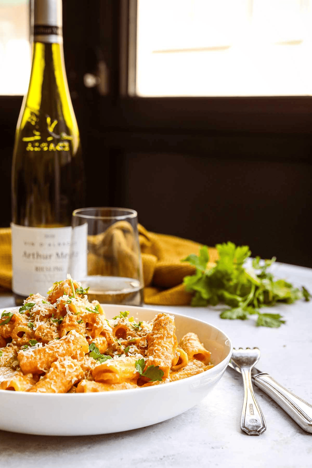 Pasta in a white dish with wine in the background