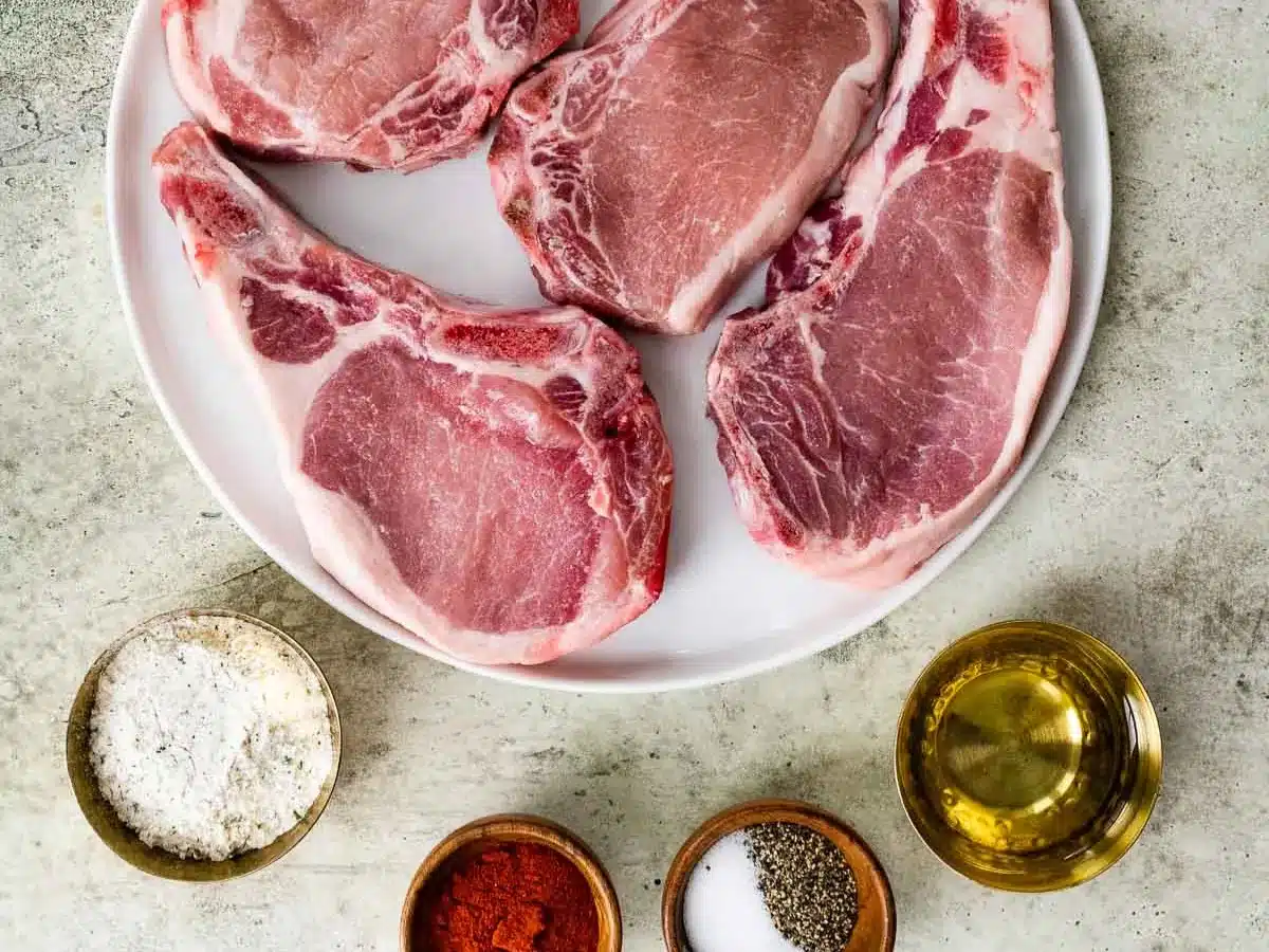 Raw pork chops on plate with measured seasonings on the side.
