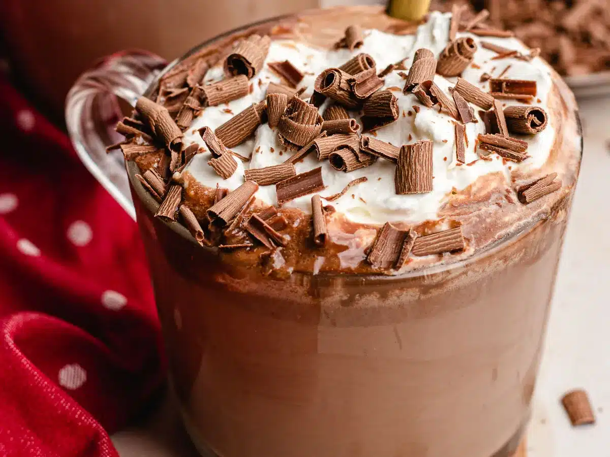 Mug with hot cocoa, topped with whipped cream and candy shavings.