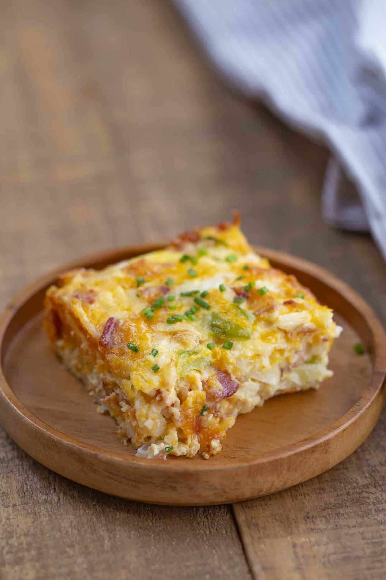Square slice of egg and bacon casserole on a wooden plate