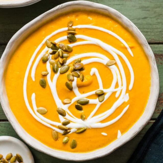 Bowl of creamy soup with creme frâiche and pumpkin seed garnish.