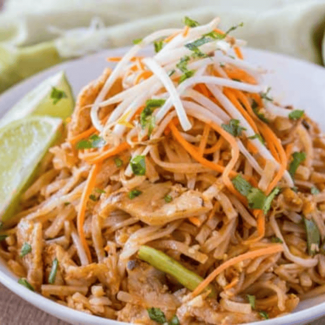 noodles and chicken topped with carrots, bean sprouts, cilantro, and served with a lime