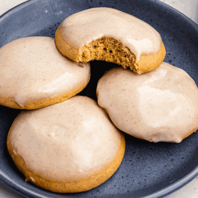 Four glazed baked cookies on plate with 1 cookie missing bite
