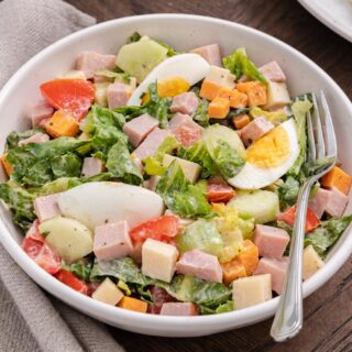 Bowl of creamy green salad with vegetables, cheese, meat, and egg.