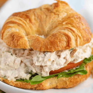 Tuna salad on a croissant with lettuce and tomato on a white plate