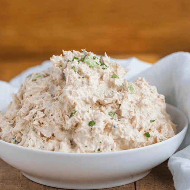 Tuna salad in a white bowl next to a white napkin on a brown table