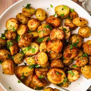Garlic Butter Roasted Potatoes finished potatoes in bowl with serving spoon.