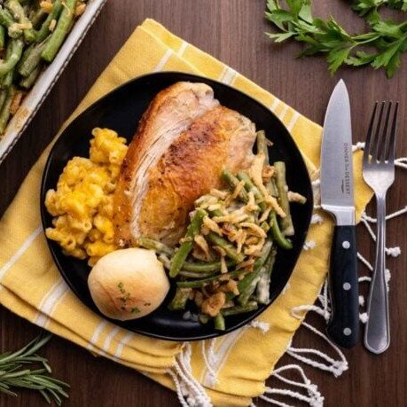Green beans with a chicken breast on a black plate with a fork and a knife