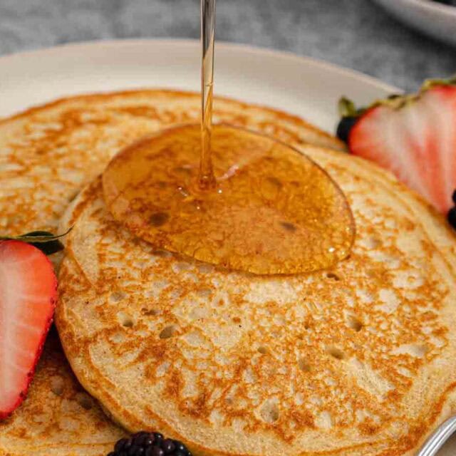 Syrup being poured on stack of pancakes.
