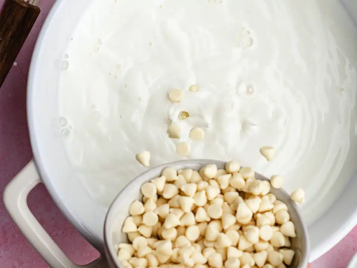 White chocolate chips being added to pot of milk.