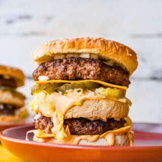 Plated double decker burger with sauce, cheese, and pickles