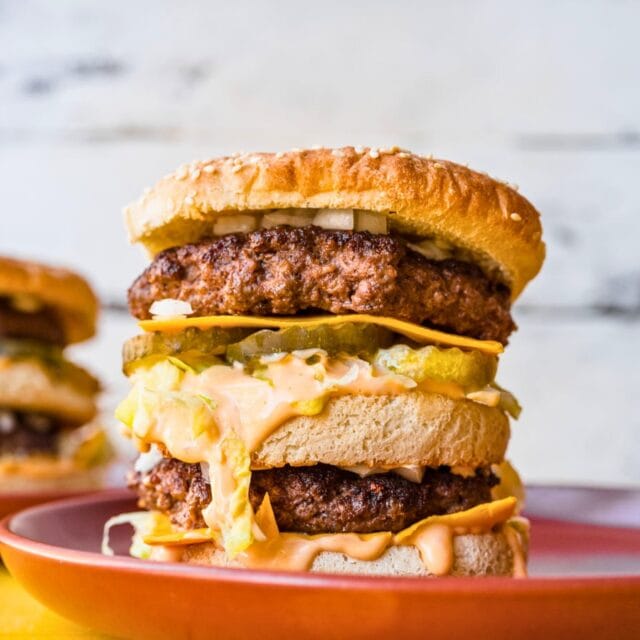 Plated double decker burger with sauce, cheese, and pickles