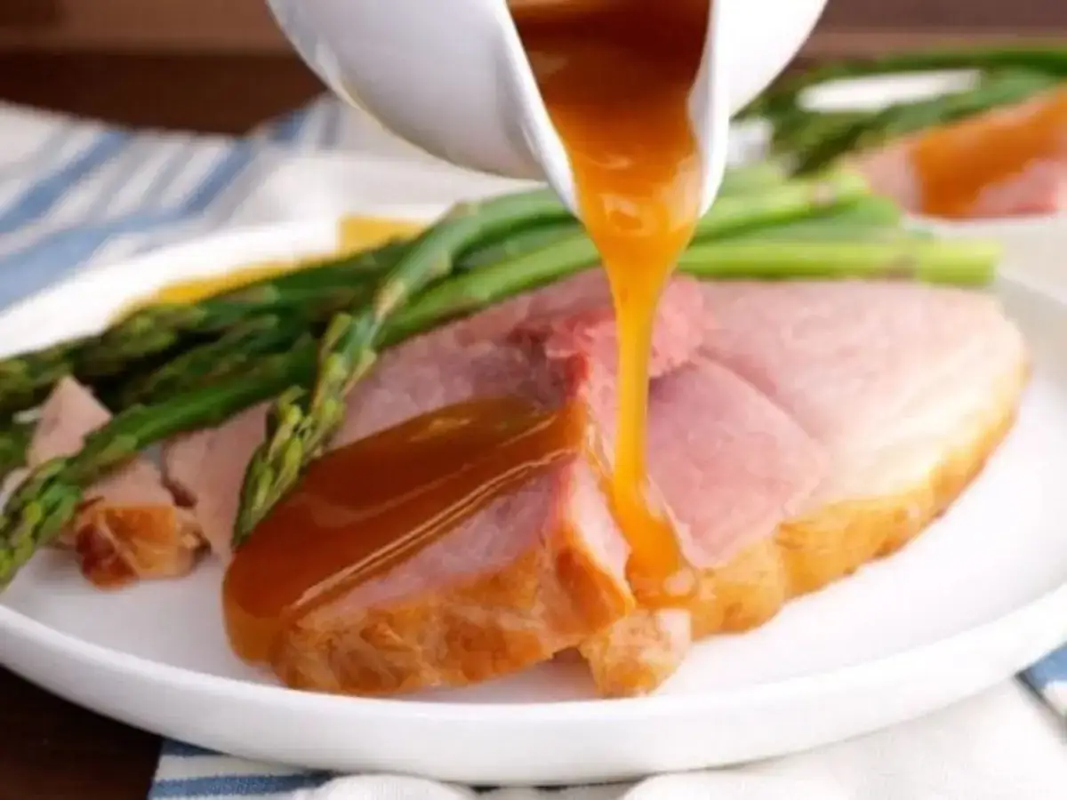 Gravy being poured on  a plate of ham