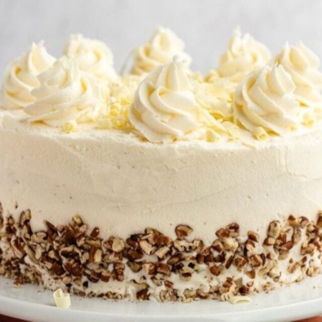 Cake on a platter garnished with pecans and frosting.