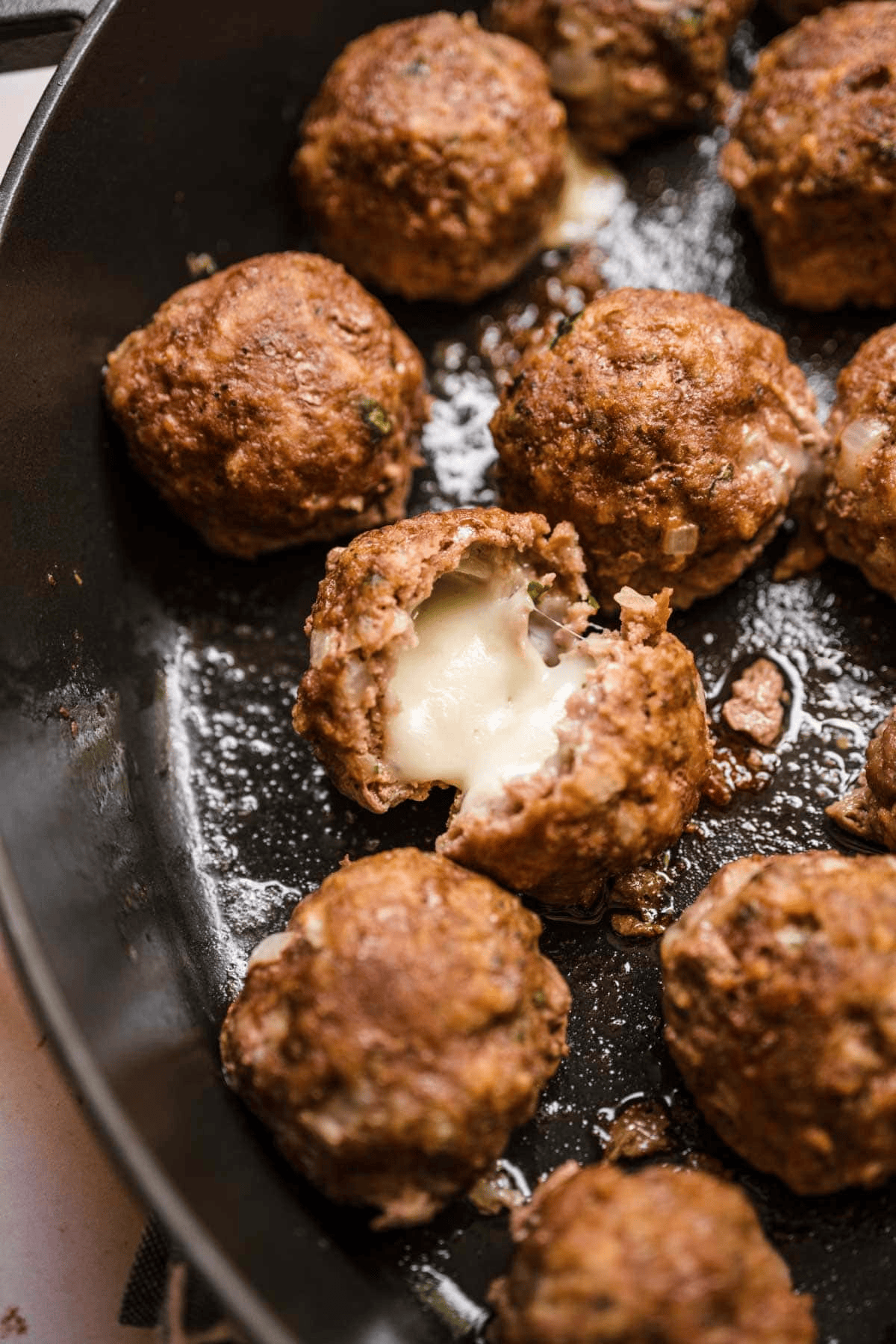 cooked meatballs in a skillet with melty cheese shown in one