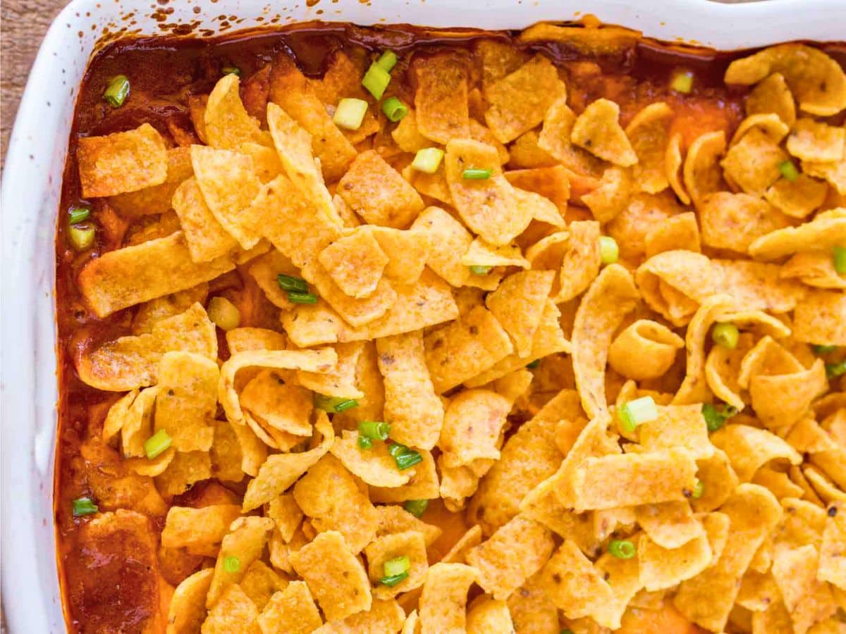 Classic Frito Pie casserole with cheese, ground beef, beans, and enchilada sauce baked with crispy Fritos on top. A childhood favorite! Top down view of baked Frito Pie in white baking dish.