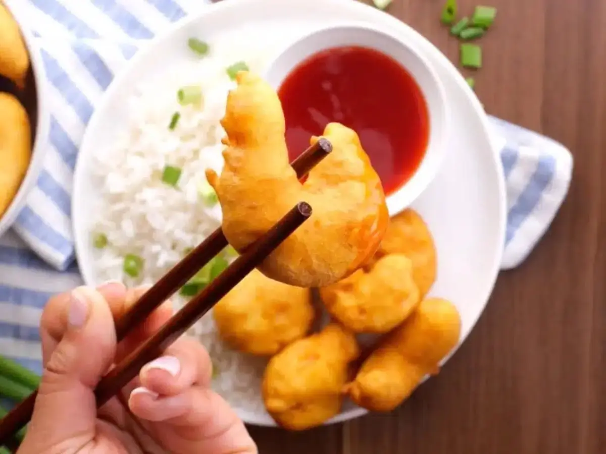 Chopsticks holding shrimp over plate of rice
