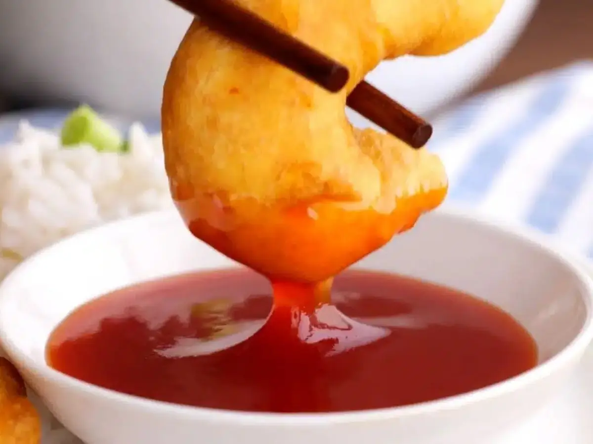 Chopsticks dipping shrimp into red sauce