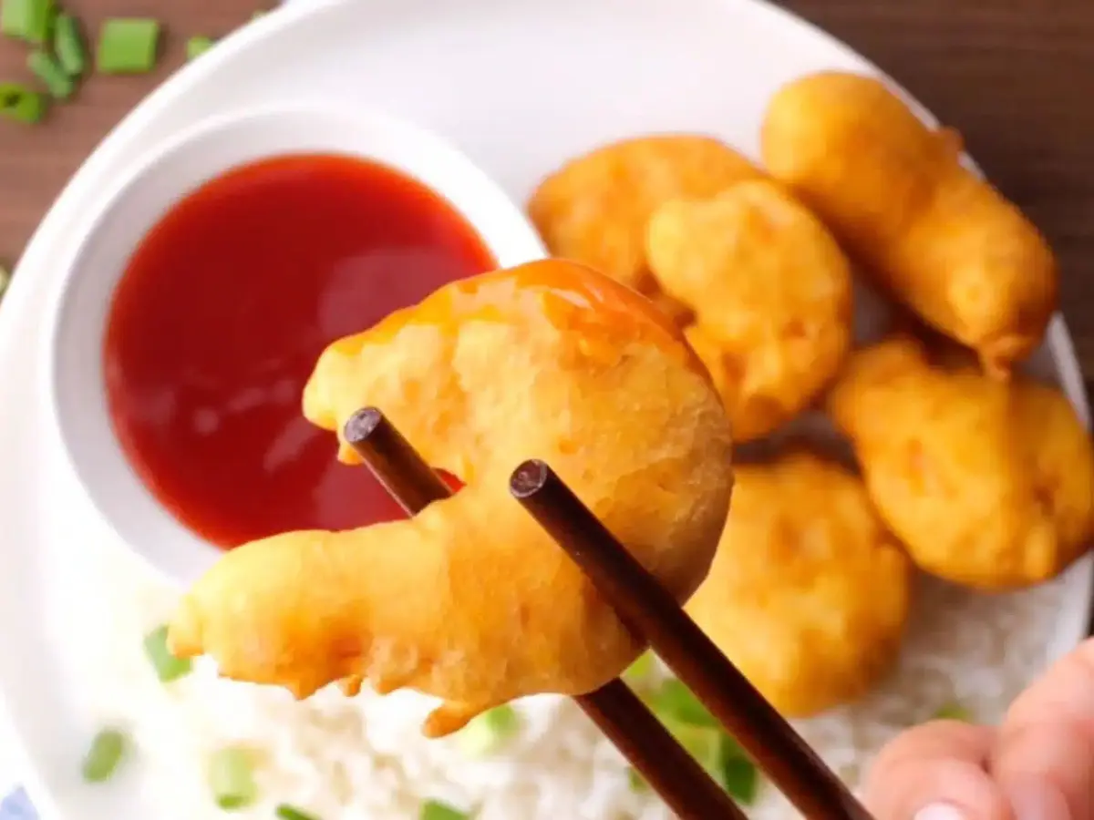 Zoomed in image of chopsticks holding shrimp over a red sauce