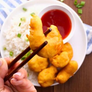 Holding shrimp with chopsticks over plated shrimp with rice and sauce.