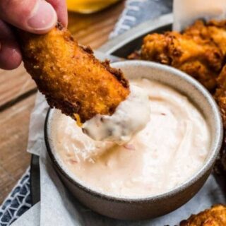 Dipping a chicken finger in the sauce.