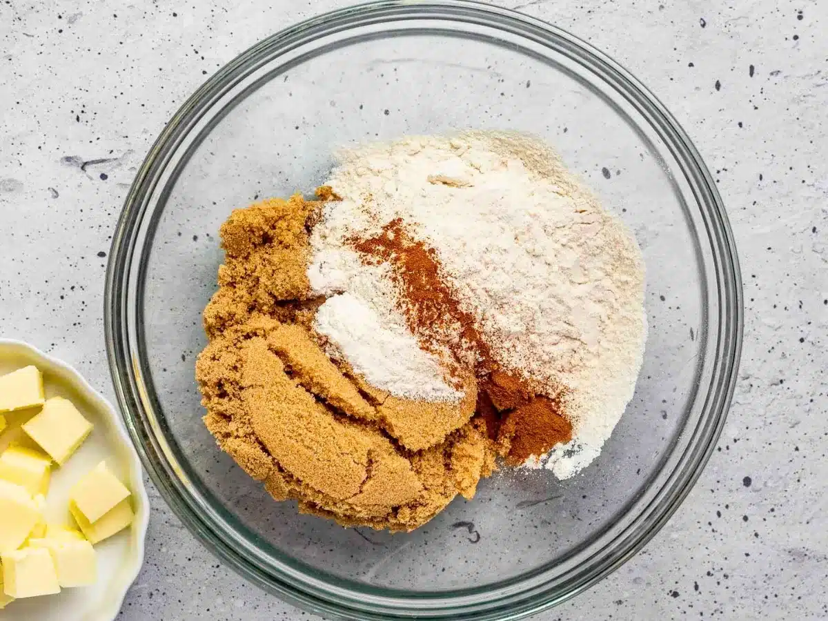 brown sugar, flour, and cinnamon in a glass bowl with squares of butter on a plate next to it