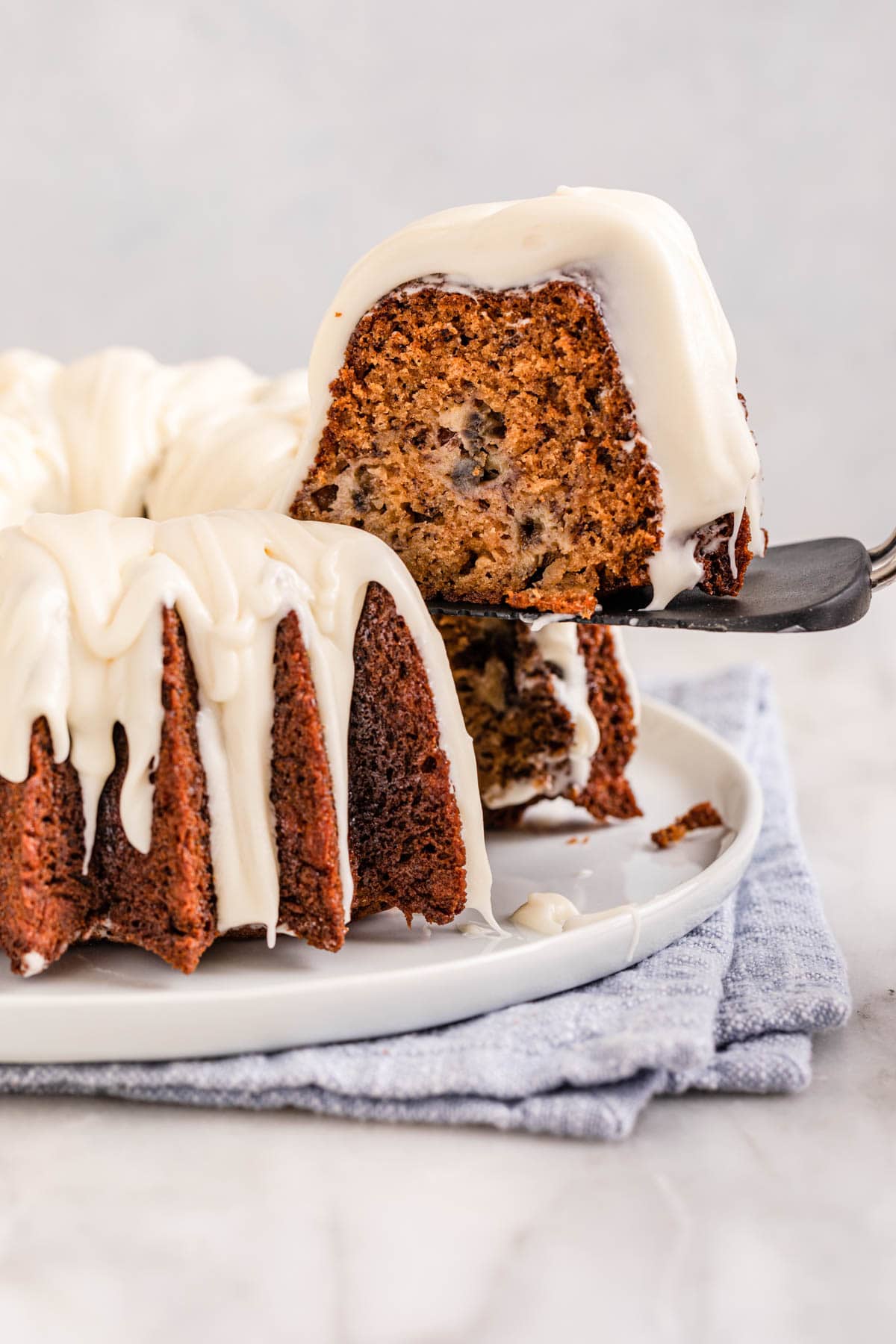 Banana Bundt Cake baked and frosted cake on plate side view, lifting slice out