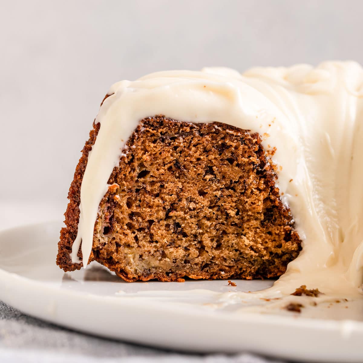 Banana Bundt Cake baked and frosted cake on plate with slice removed, side view