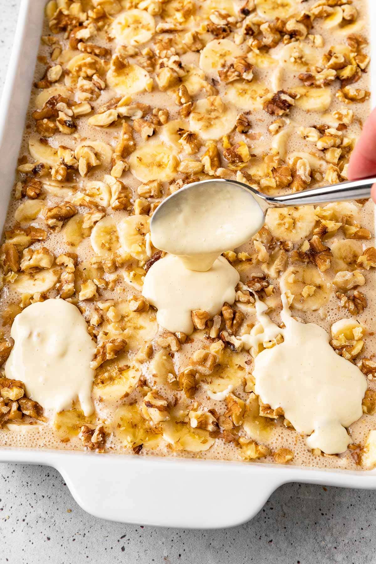 Bananas Foster Cobbler in baking pan before cooking spooning cream cheese topping over it