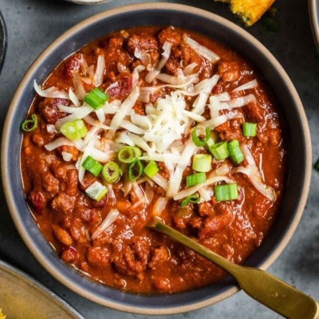 Chili in a bowl with cheese, green onions and a spoon.