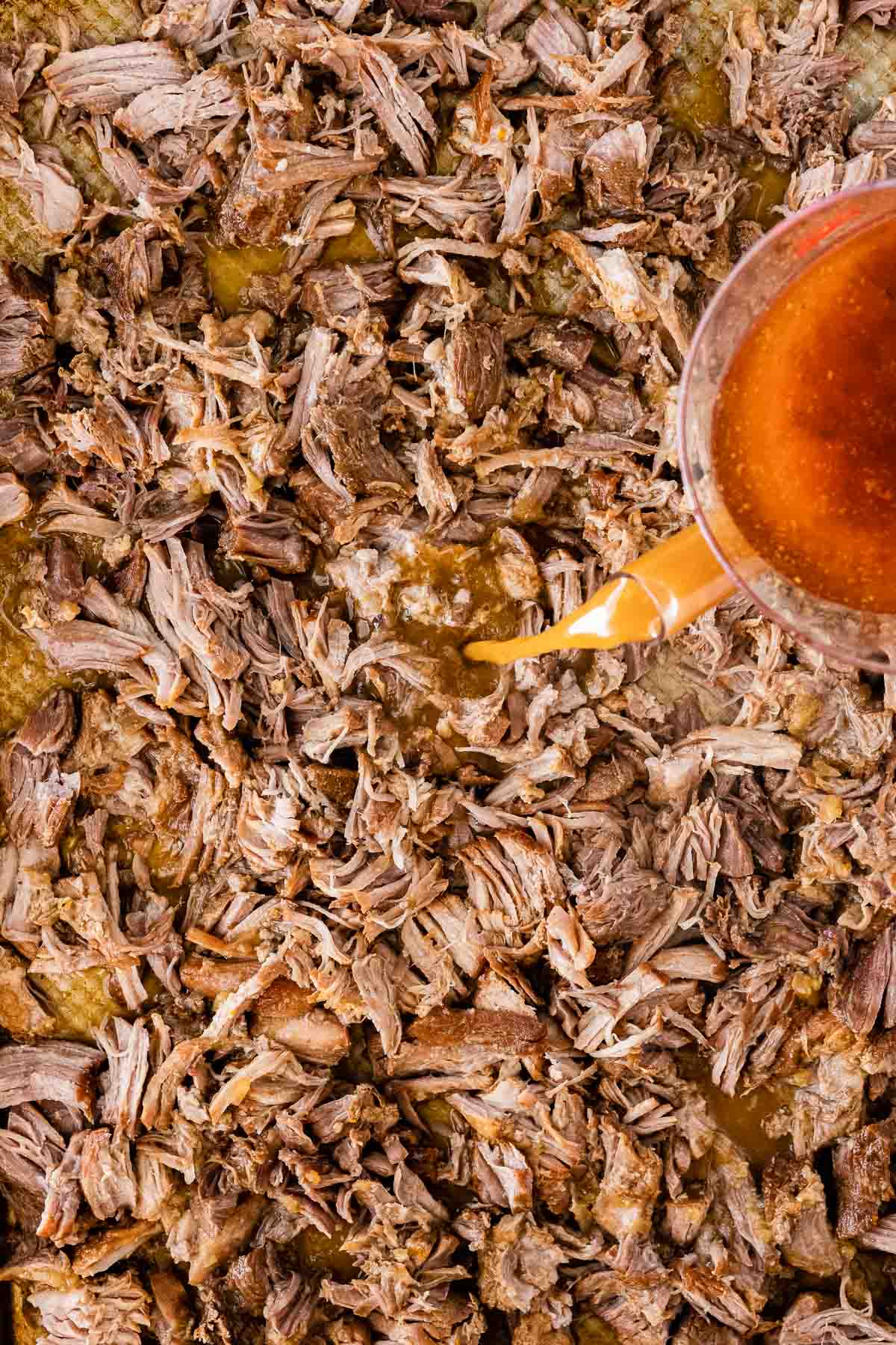 Instant Pot Pork Carnitas pouring cooking juices over shredded meat on baking tray