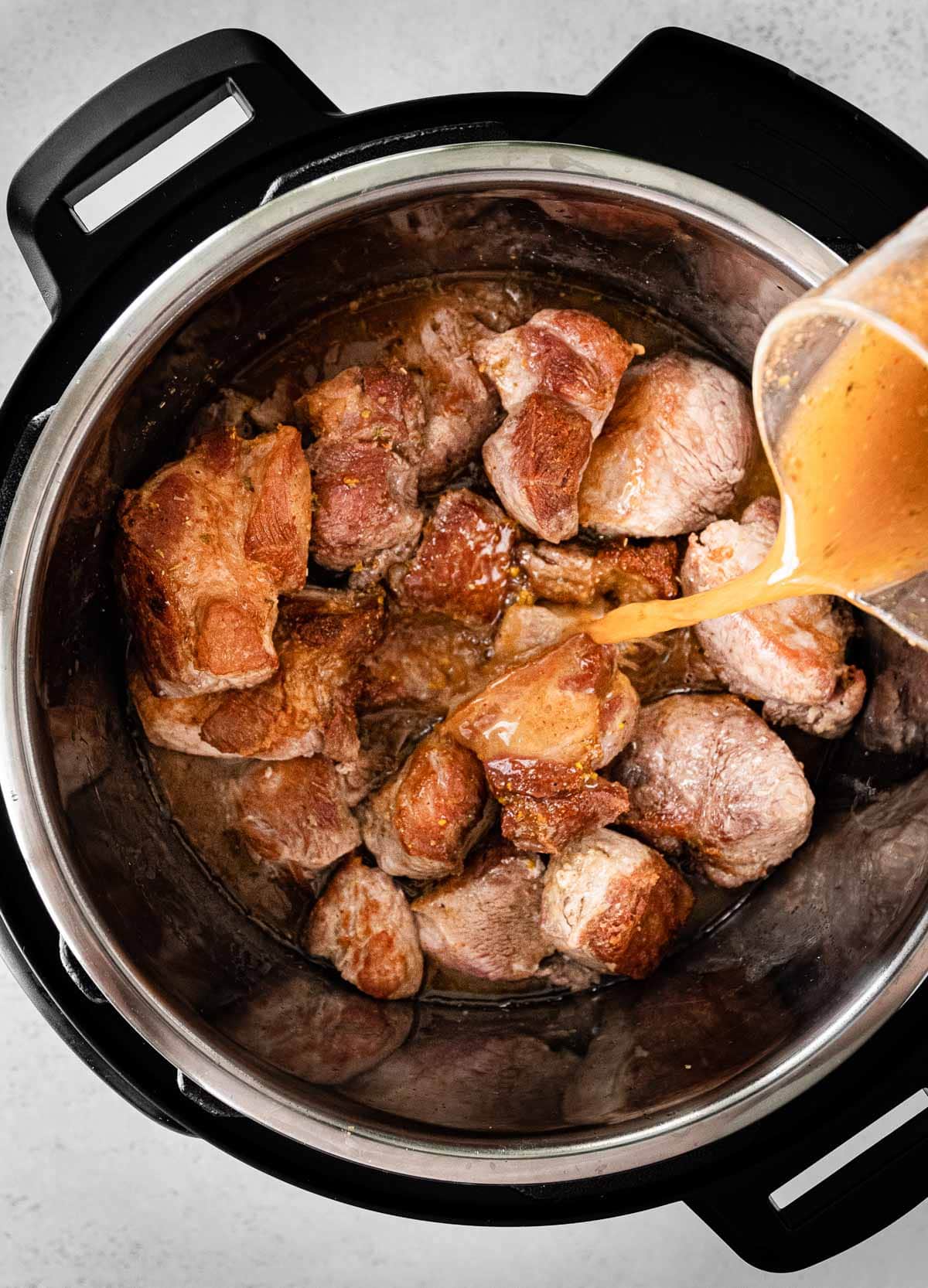 Instant Pot Pork Carnitas adding cooking liquid over seared pork pieces in instant pot