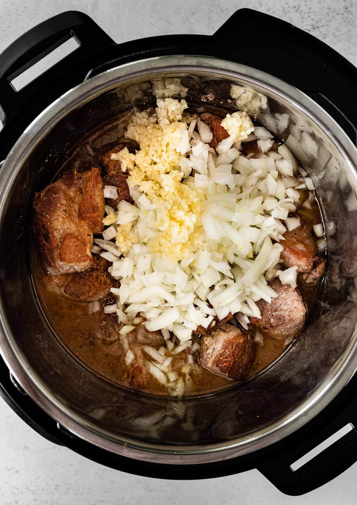 Instant Pot Pork Carnitas adding onions and garlic over meat in instant pot