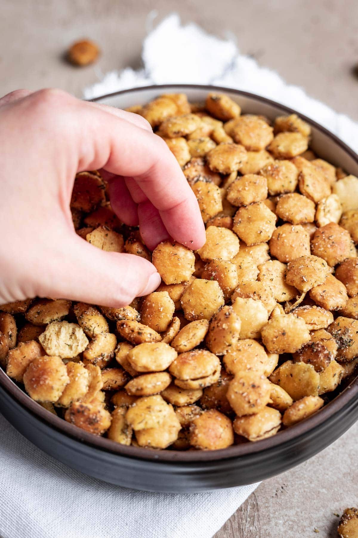 Ranch Oyster Crackers seasoned and baked in a large bowl and hand grabbing a portion
