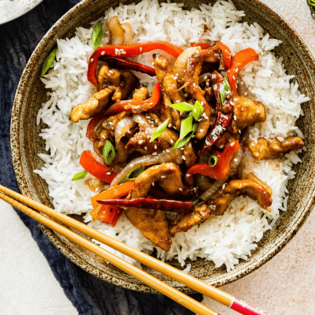 chicken and veggies on a bed of rice in a bowl with chopsticks
