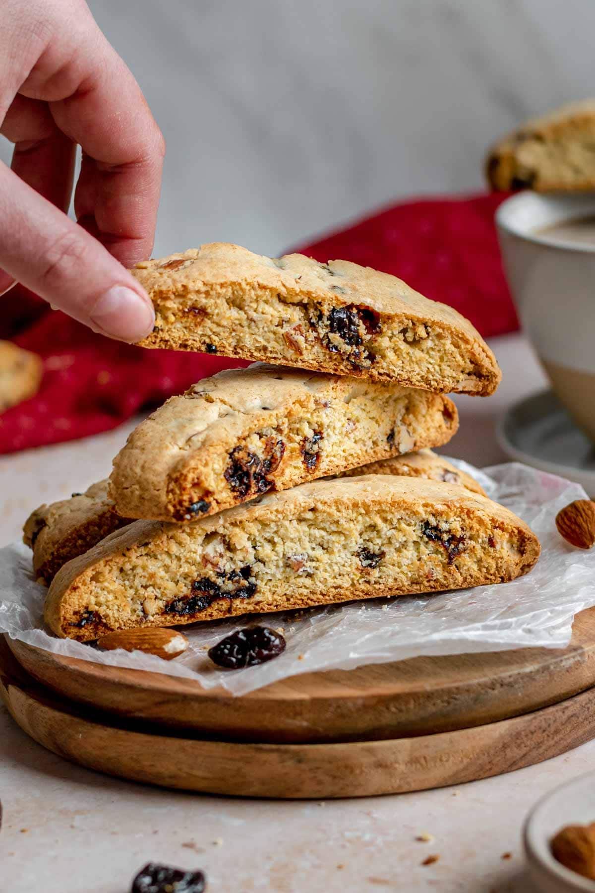 Cherry Almond Biscotti cookies stacked on plate with hand grabbing top cookie