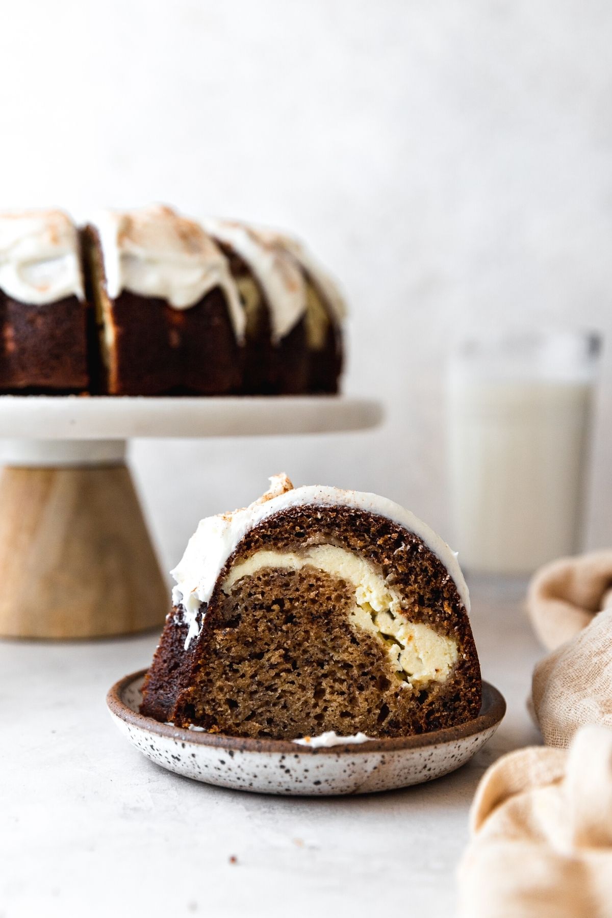 Banana Cheesecake Bundt Cake finished slice on plate with cake on cake stand in background