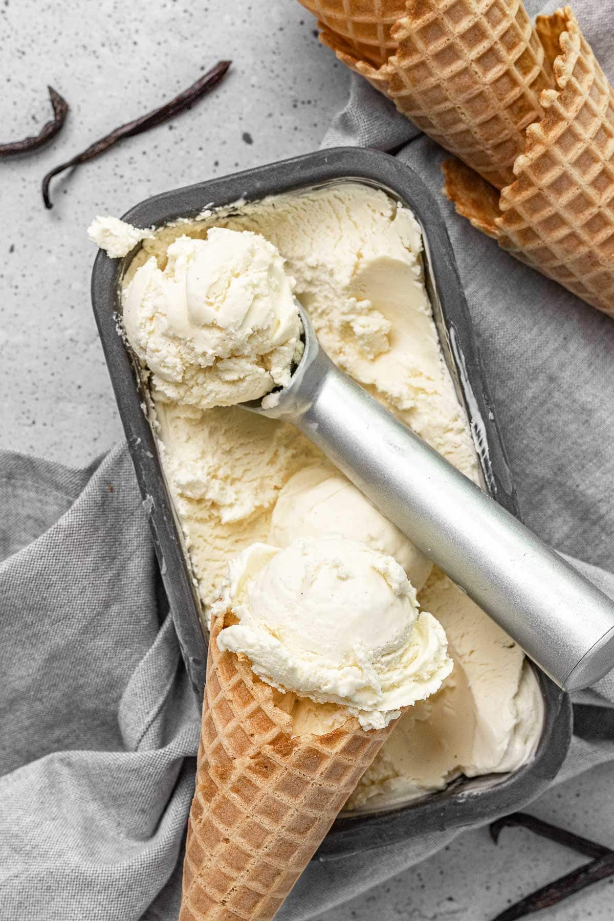 French Vanilla Ice Cream finished in loaf pan with ice cream scoop and scoop in waffle cone on top,