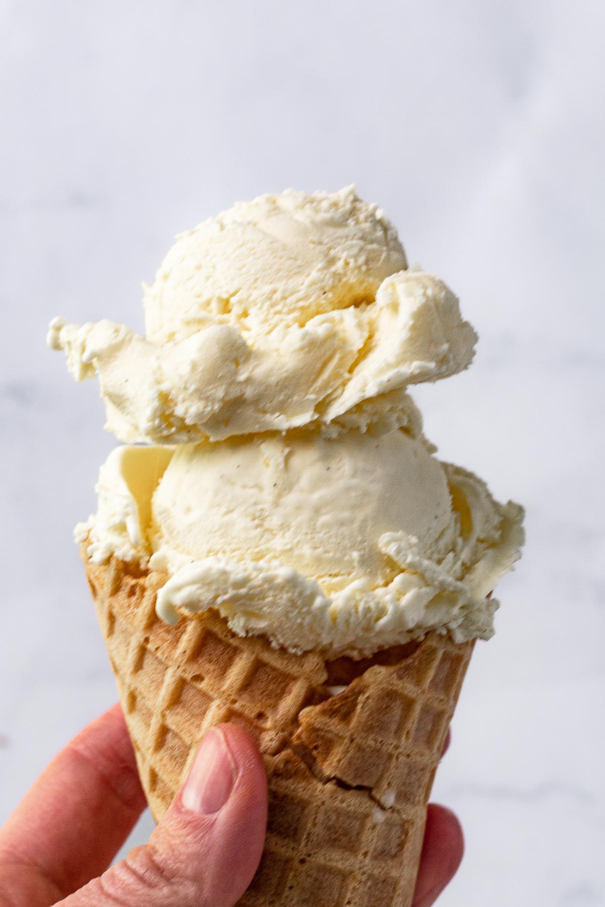 French Vanilla Ice Cream hand holding waffle cone with two scoops of ice cream