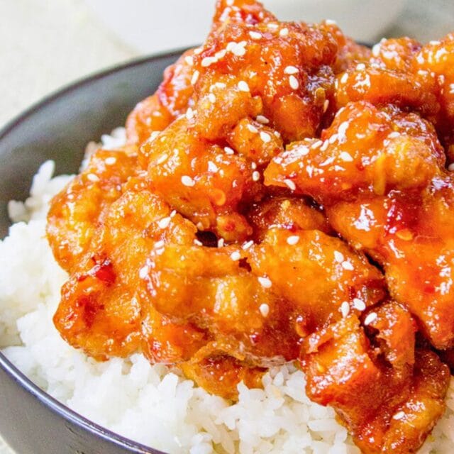 Saucy chicken pieces over white rice in bowl