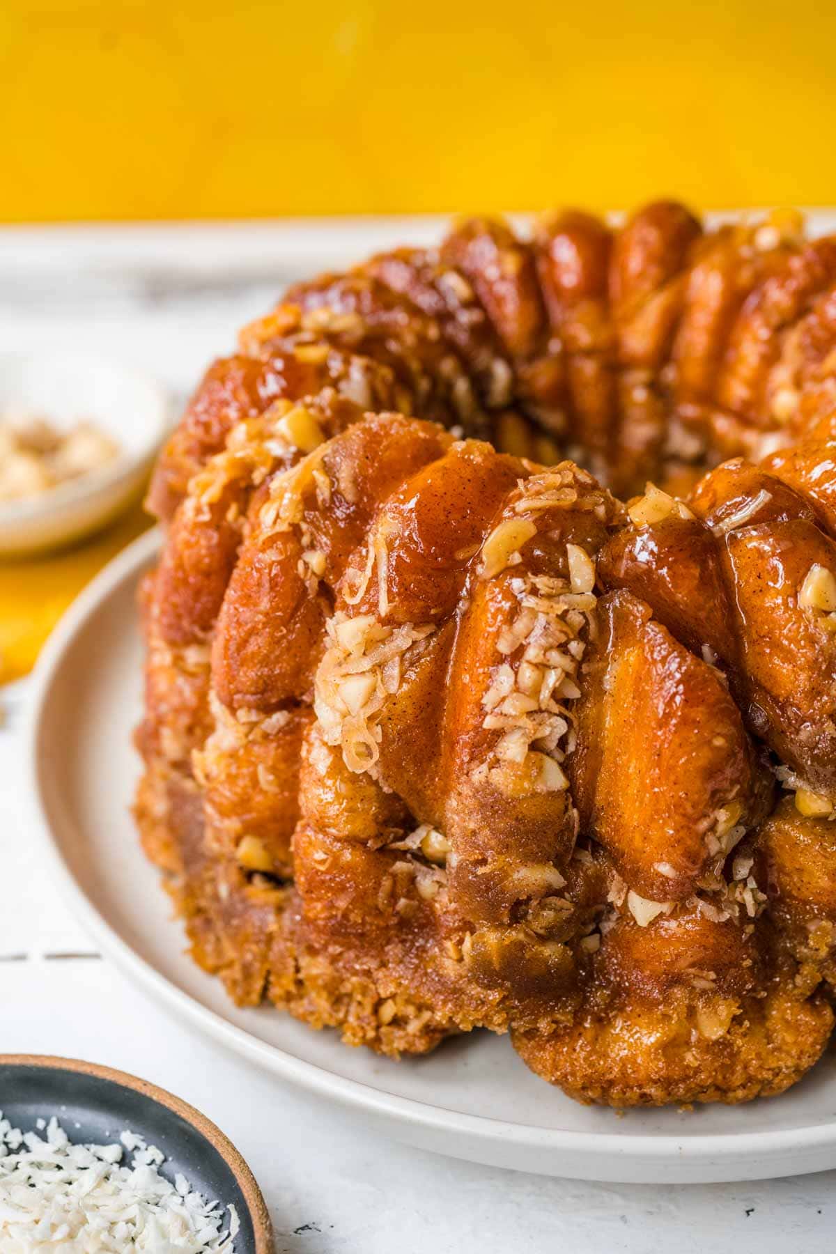 Hawaiian Monkey Bread finished on plate with coconut shreds and macadamia nuts in small bowls next to plate